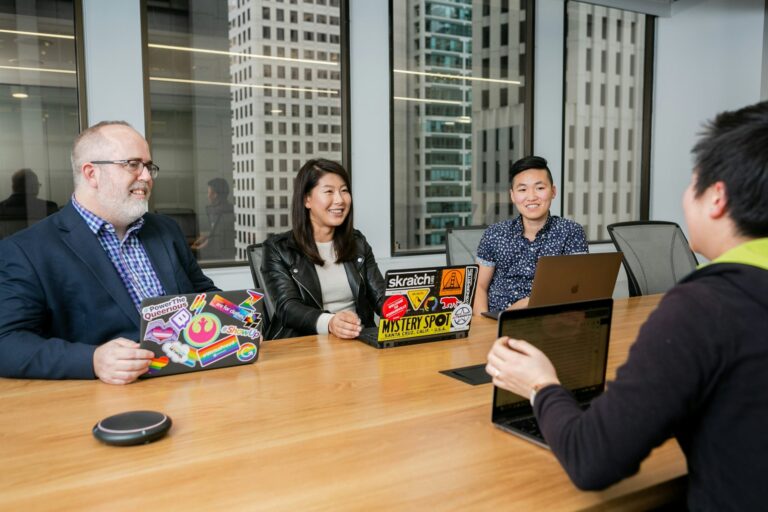 Meeting of people with laptops covered in stickers in a highrise boardroom